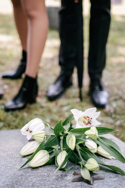 A bouquet of white lilies with large, open blooms and closed buds is arranged on a stone surface, featuring lush green leaves. The flowers appear fresh with smooth, velvety petals and sturdy stems. In